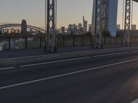 a car traveling down an empty highway near a bridge at sunset, with skyscrapers and buildings in the background