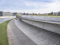 a concrete walkway on a river bank with several buildings in the background and a bike path