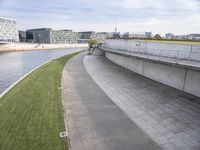 a concrete walkway on a river bank with several buildings in the background and a bike path