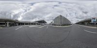 a road with a few cars at the curb by some buildings and a sky with clouds