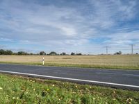 a road leading to a large open field with power lines overhead and a sign warning that the power lines are closed