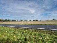 a road leading to a large open field with power lines overhead and a sign warning that the power lines are closed