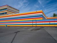 an empty parking lot painted brightly stripes on the wall of the building and sky as well as stones