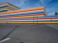 an empty parking lot painted brightly stripes on the wall of the building and sky as well as stones