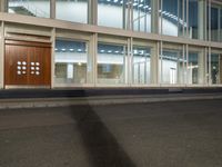 a tall brown wooden door sitting inside of a window filled office building, with some lights on