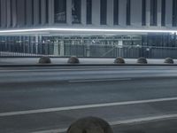 the empty city road is empty by the tall building in the background at night with light streaking on the buildings