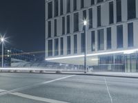 the empty city road is empty by the tall building in the background at night with light streaking on the buildings