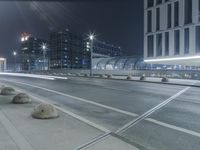 the empty city road is empty by the tall building in the background at night with light streaking on the buildings