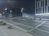 the empty city road is empty by the tall building in the background at night with light streaking on the buildings