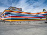 an empty parking lot painted brightly stripes on the wall of the building and sky as well as stones