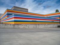 an empty parking lot painted brightly stripes on the wall of the building and sky as well as stones