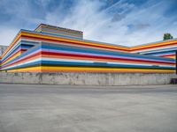 an empty parking lot painted brightly stripes on the wall of the building and sky as well as stones