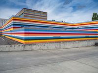 an empty parking lot painted brightly stripes on the wall of the building and sky as well as stones