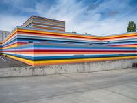 an empty parking lot painted brightly stripes on the wall of the building and sky as well as stones