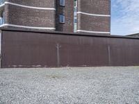 a rusty metal fence with a large building in the background in the background is a gray gravel field