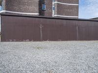 a rusty metal fence with a large building in the background in the background is a gray gravel field