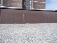 a rusty metal fence with a large building in the background in the background is a gray gravel field