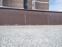 a rusty metal fence with a large building in the background in the background is a gray gravel field