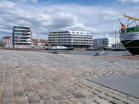 a large green boat sitting on top of a brick street next to buildings and water