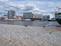 a large green boat sitting on top of a brick street next to buildings and water