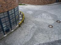 an aerial view of a brick building with yellow post markers lining the street that goes up from the outside