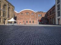 a brick street with a couple buildings in the background that include several white tents to protect against the sun