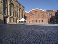 a brick street with a couple buildings in the background that include several white tents to protect against the sun