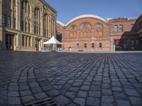 a brick street with a couple buildings in the background that include several white tents to protect against the sun