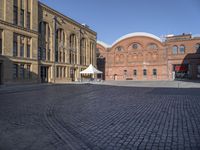 a brick street with a couple buildings in the background that include several white tents to protect against the sun