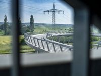 a long wooden bridge over a valley next to green grass and electricity poles are overhead