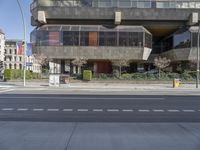 empty intersection in city with large concrete building behind it and traffic lights along side it