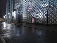 a walkway and building at night on a city street with a puddle of rain and wet pavement