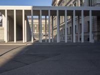 the large, empty sidewalk with multiple columns in front of the building with two signs