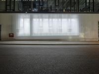 an empty street with large windows and drapes outside of it by a city curb