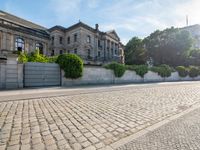 a cobblestone road leads up the side of this building where there are many bushes in front