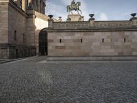 an image of the back of a castle entrance on cobblestone pavement near a statue