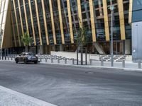 a black car driving down the road in front of a big building that has a lot of tall buildings in it