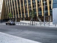 a black car driving down the road in front of a big building that has a lot of tall buildings in it