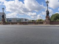 two street lights on a bridge over an empty street with buildings in the background,