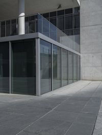 the glass enclosed building has stairs and a railing on one side of it and a concrete building behind it