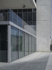 the glass enclosed building has stairs and a railing on one side of it and a concrete building behind it