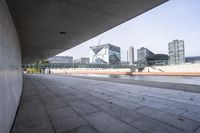 an empty walkway next to a lake in the middle of the city with tall buildings