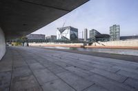 an empty walkway next to a lake in the middle of the city with tall buildings