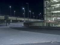 a parking lot with several lights along a street and an empty sidewalk near it at night