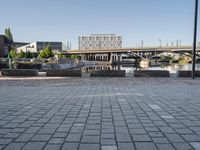 an empty street with some benches and a bridge over a waterway in the background and in the foreground, in a large square brick pattern