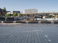 an empty street with some benches and a bridge over a waterway in the background and in the foreground, in a large square brick pattern