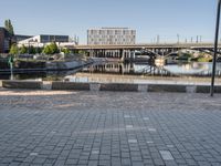 an empty street with some benches and a bridge over a waterway in the background and in the foreground, in a large square brick pattern