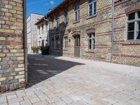 an empty stone courtyard between two large brick buildings, with a blue sky above it