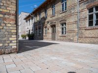 an empty stone courtyard between two large brick buildings, with a blue sky above it