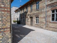 an empty stone courtyard between two large brick buildings, with a blue sky above it